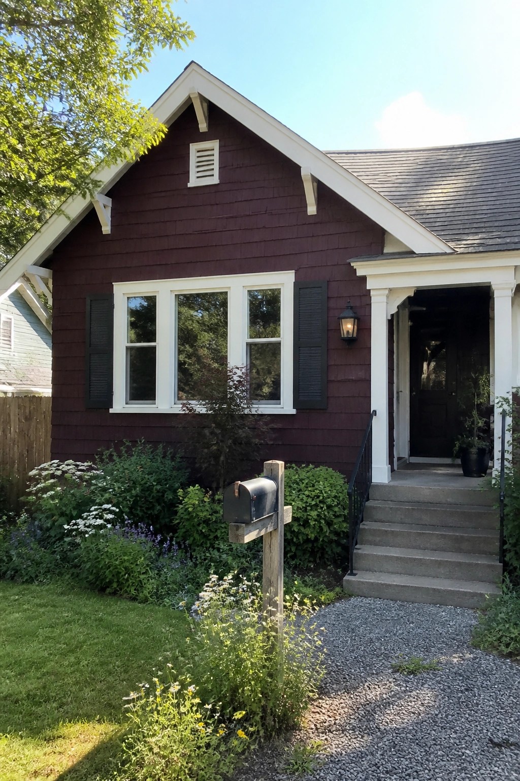 A deep burgundy house exterior with black shutters, white trim, a covered porch, and a gravel path leading to the front steps.