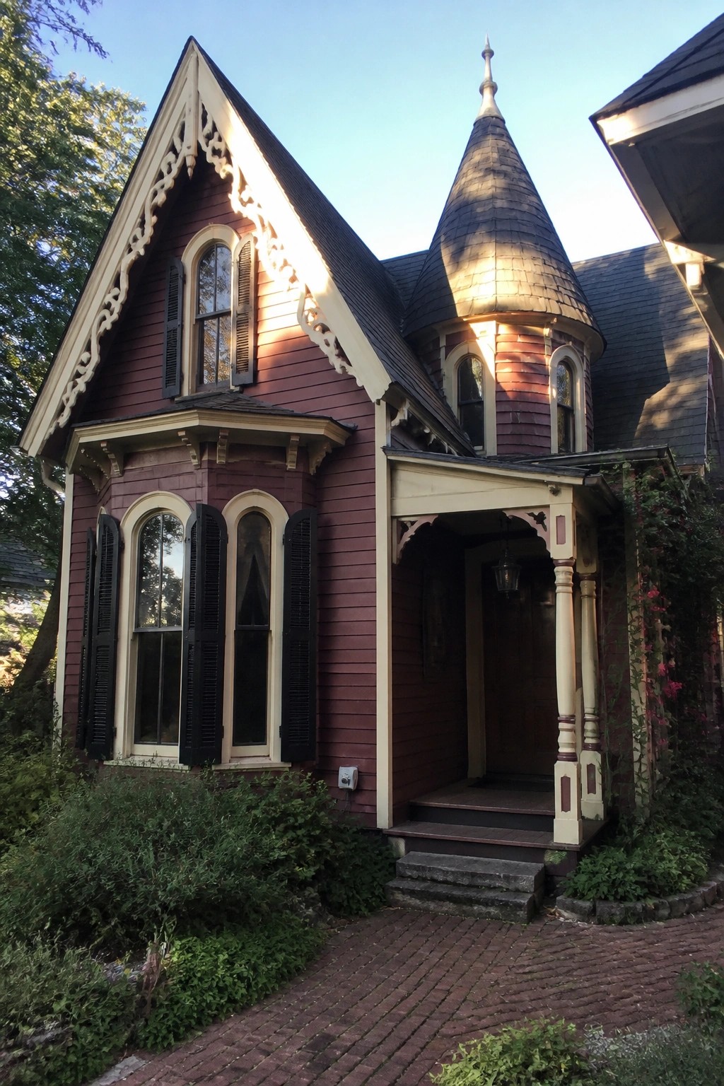 Maroon Victorian house with turret, ornate trim, black shutters, and brick path