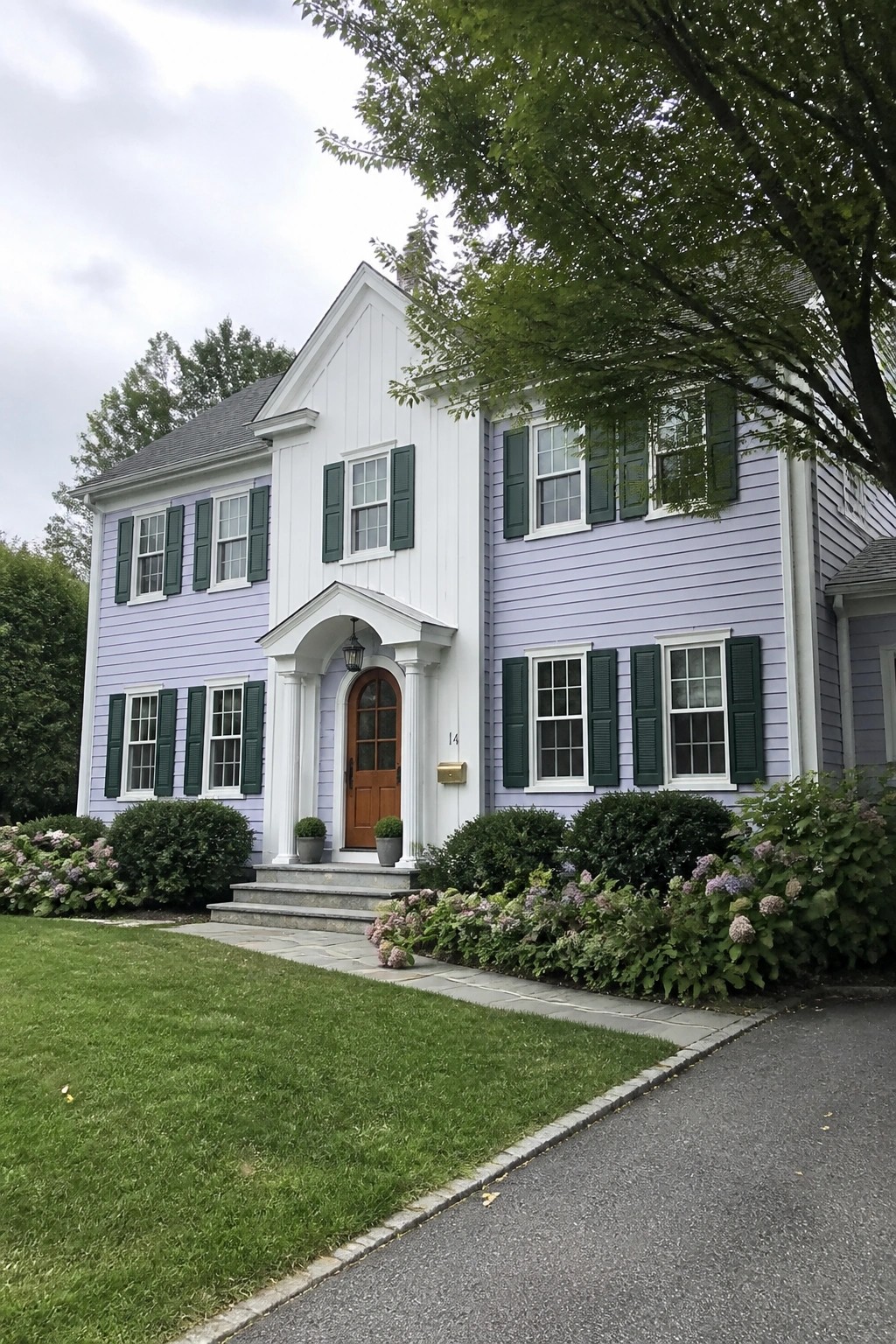 A two-story house with light purple siding, white board-and-batten on the gable and entry, green shutters, and a brown door.