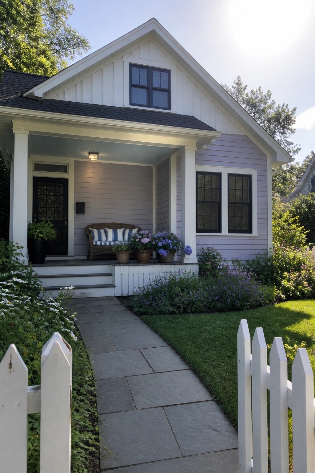 Charming lavender house with white porch, wicker bench, potted flowers, and stone path.