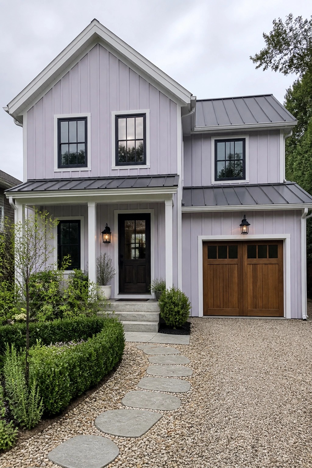 A two-story house with light purple vertical siding, white trim, a dark front door, wooden garage doors, and a gravel driveway with a stone path.