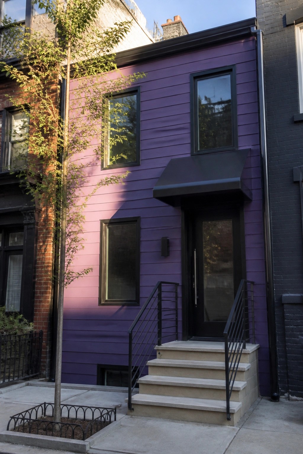 A narrow two-story house covered in deep purple horizontal lap siding with black window frames, a black front door, and concrete steps leading to the entrance.