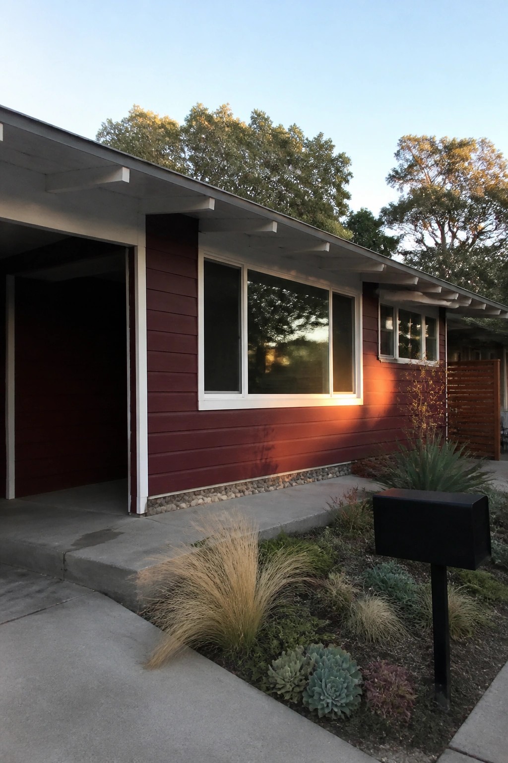 Red mid-century house with large windows, open carport, mailbox, and succulent garden.