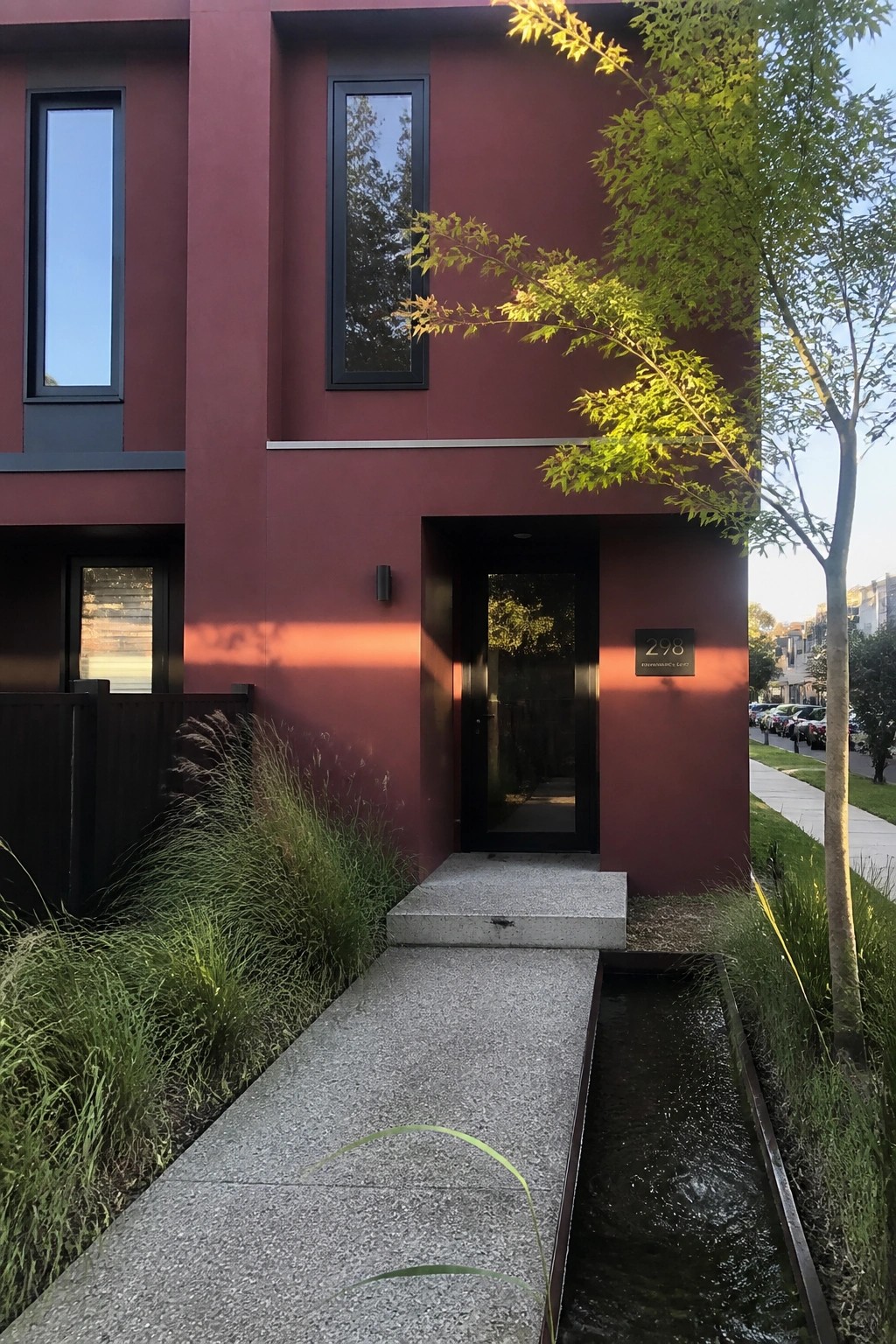 Red modern building with black door 298, concrete path, and water channel.