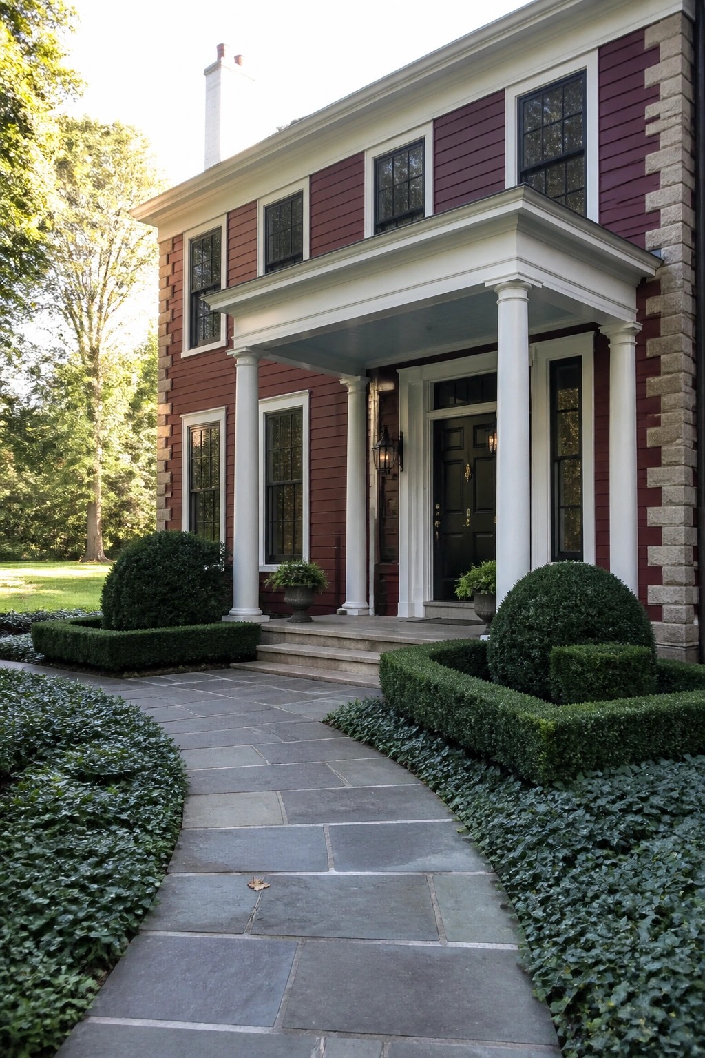 A two-story house with burgundy siding, white trim and columns, a covered entry porch, and a stone path leading to the front door.