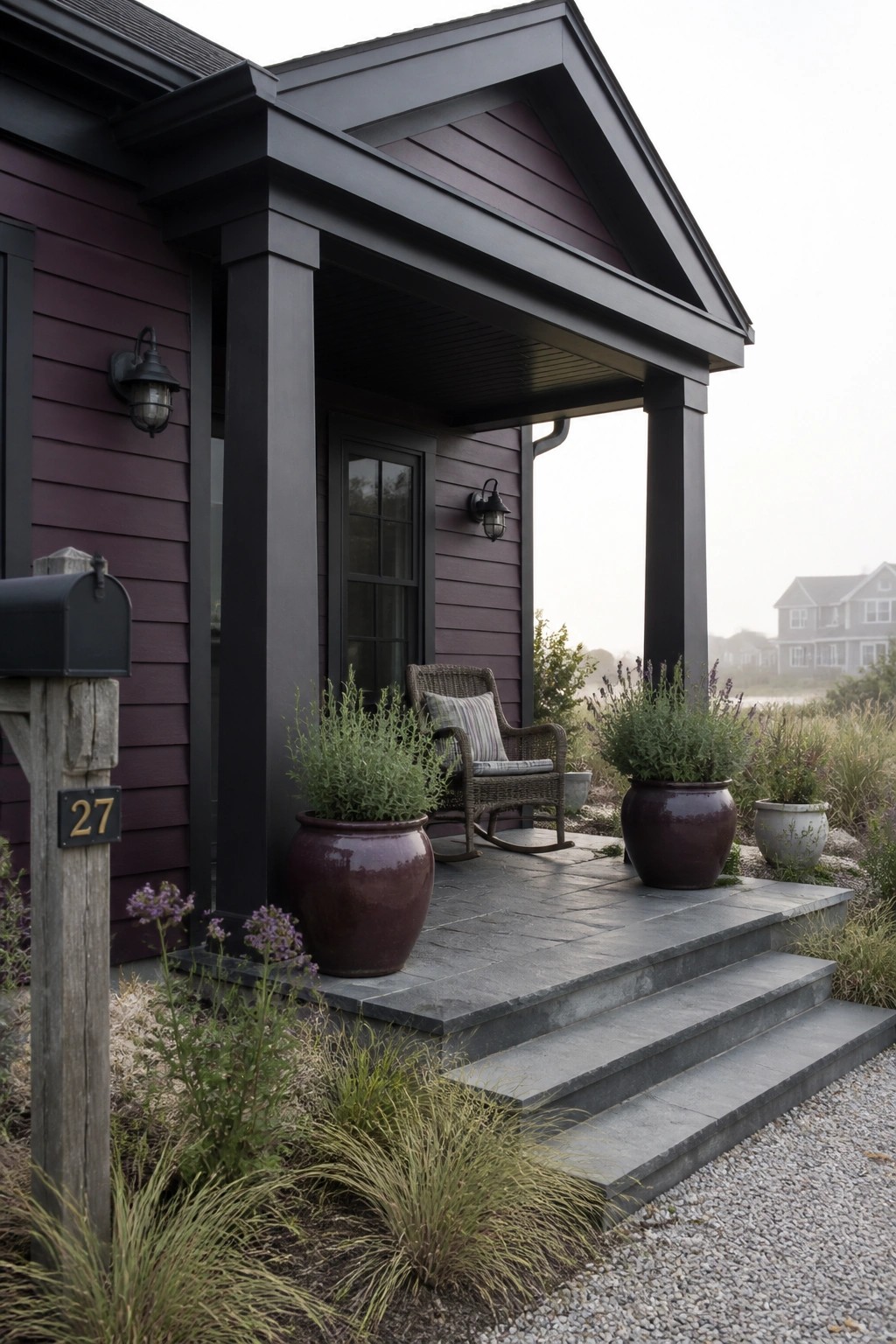 A dark purple house with black trim and posts, a covered porch with stone steps, and large planters beside the entrance.