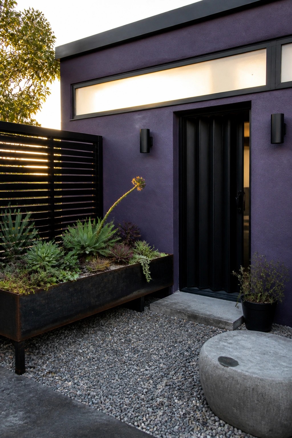 A deep purple house exterior with black trim, a black front door, a raised metal planter filled with succulents, and a gravel courtyard area.