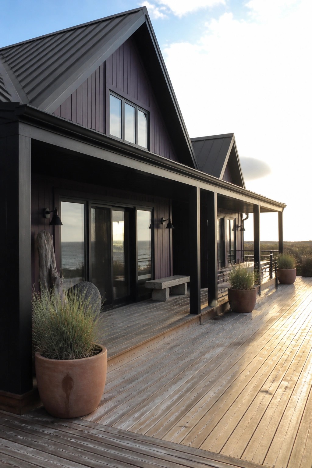 A modern house with dark purple siding, black trim, large windows, and a wooden deck facing the ocean.