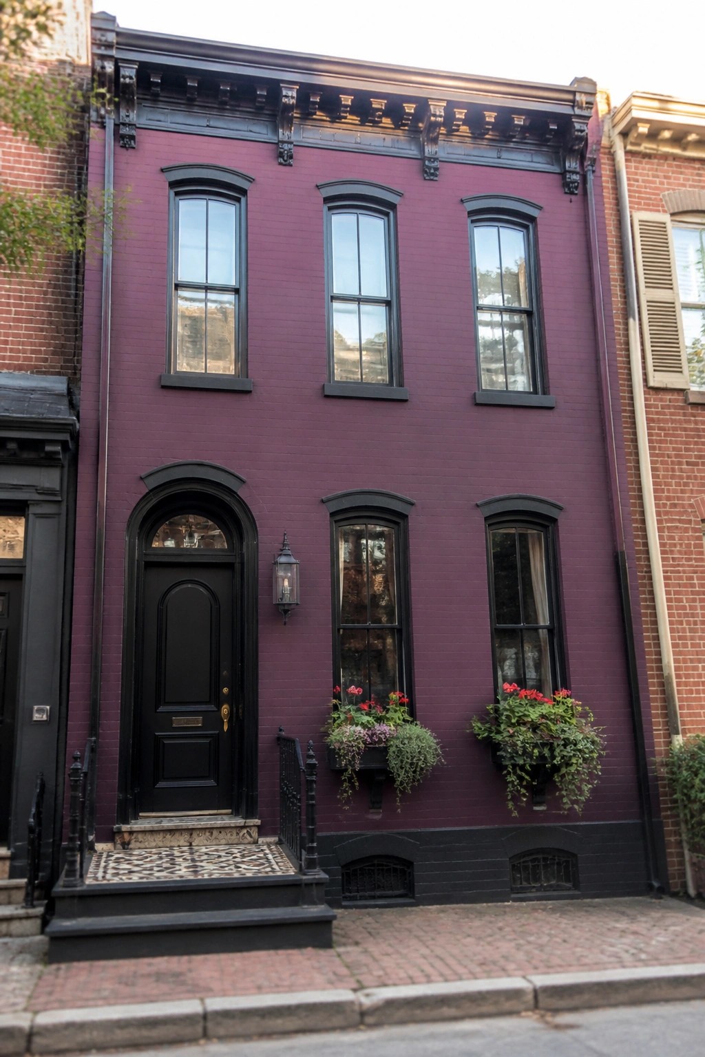 A narrow three-story row house painted deep purple with black trim, an arched front door, three second-floor windows, and flower boxes on the ground floor.