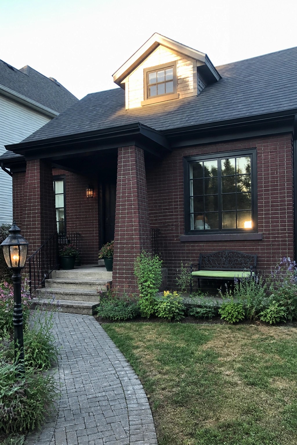 Red brick house with porch, bench, dormer window, and garden pathway at dusk.