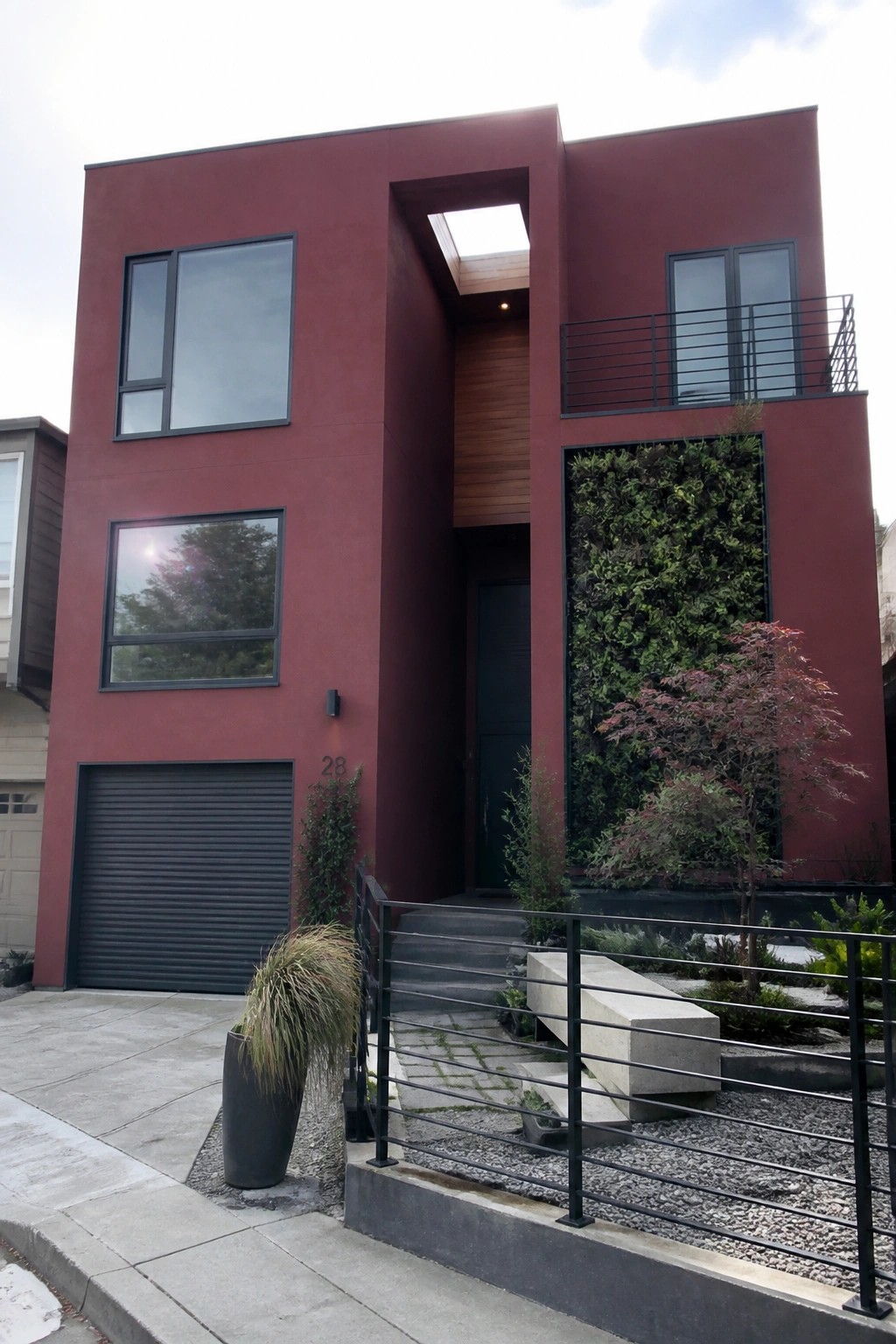 Modern red house with vertical green wall, dark windows, garage, and steps.