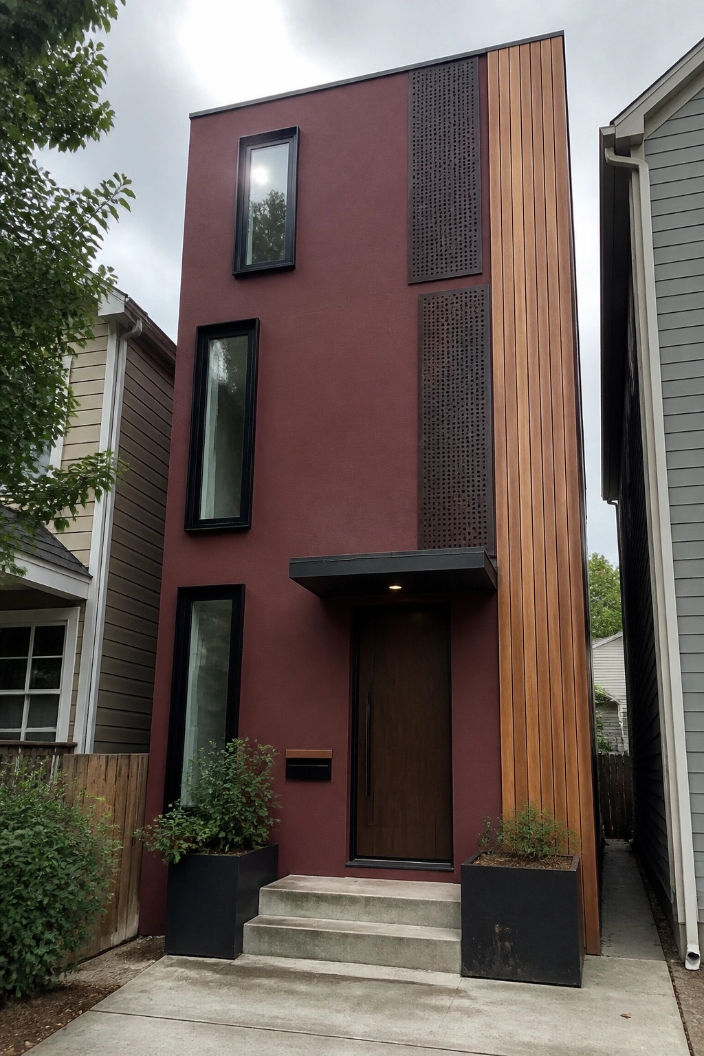 Modern narrow townhouse with maroon facade, wood paneling, black windows, and concrete steps.