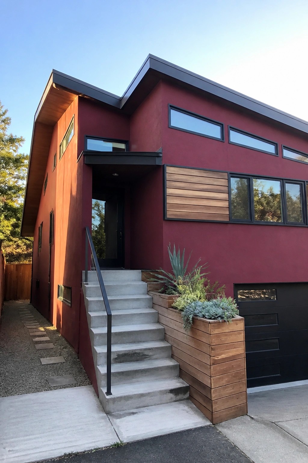 Modern red house with concrete stairs, wooden planter, black windows and garage.