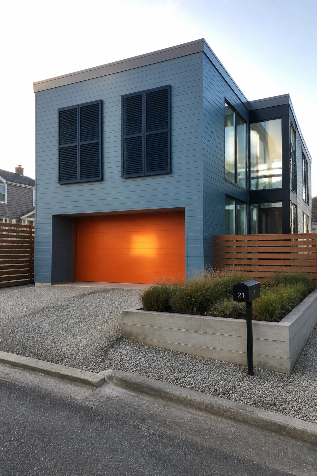 Modern blue house with bright orange garage door, large windows, and gravel driveway.