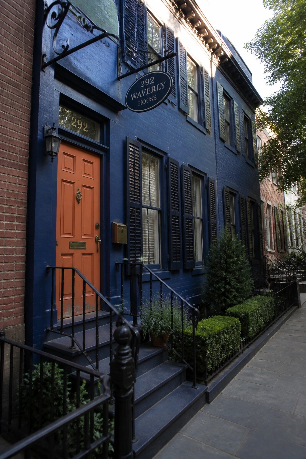 A navy blue row house with an orange front door, navy shutters, black railings, and a sign for 292 Waverly House.