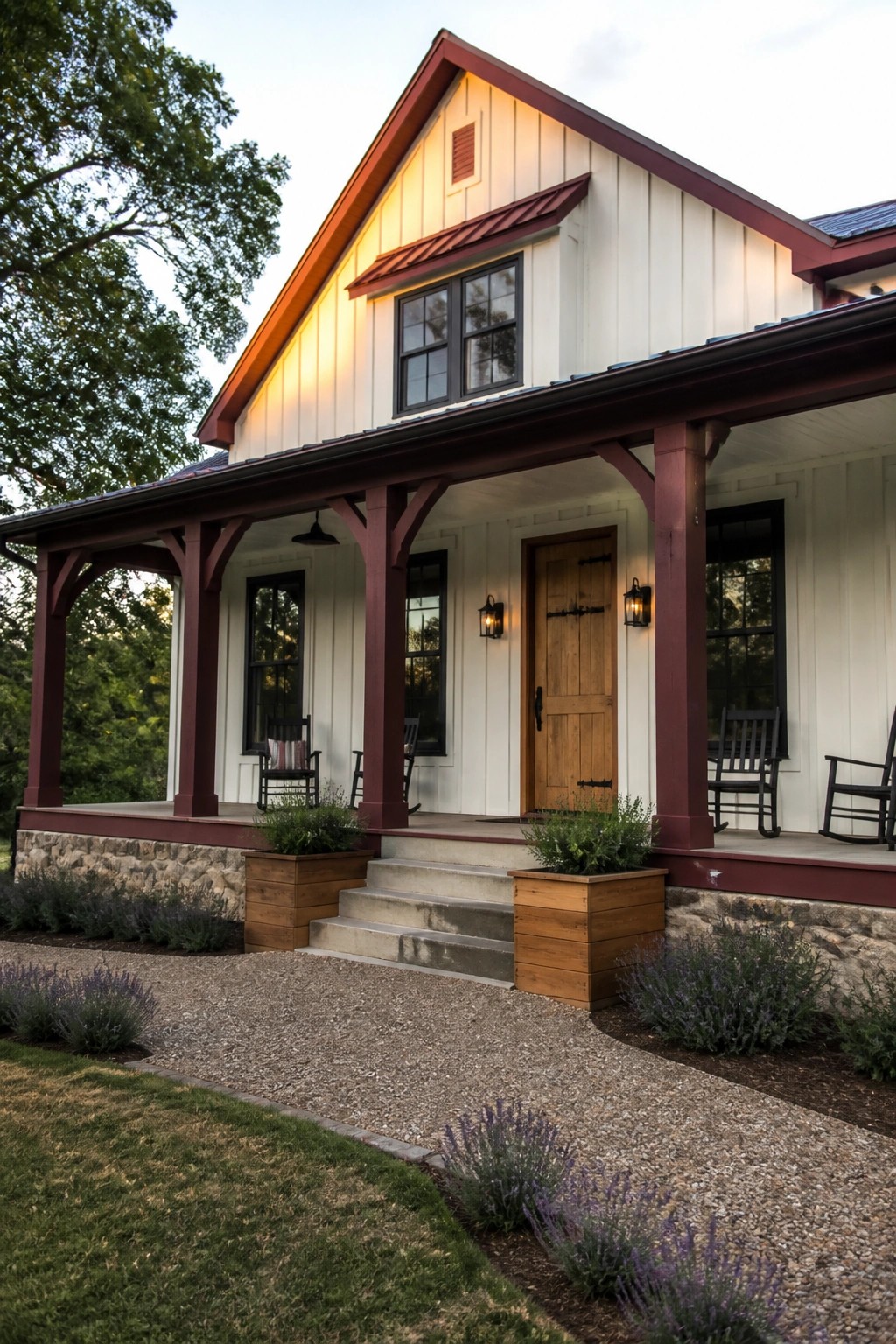 Front view of a white board-and-batten house with maroon trim, porch posts, and metal roof accents, including a wooden door and rocking chairs on the porch.