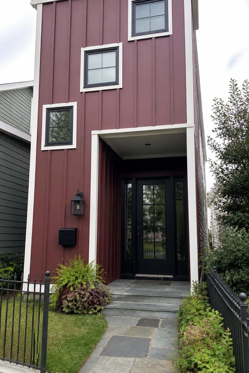 Maroon house with black door, white trim, stone walkway, and green plants