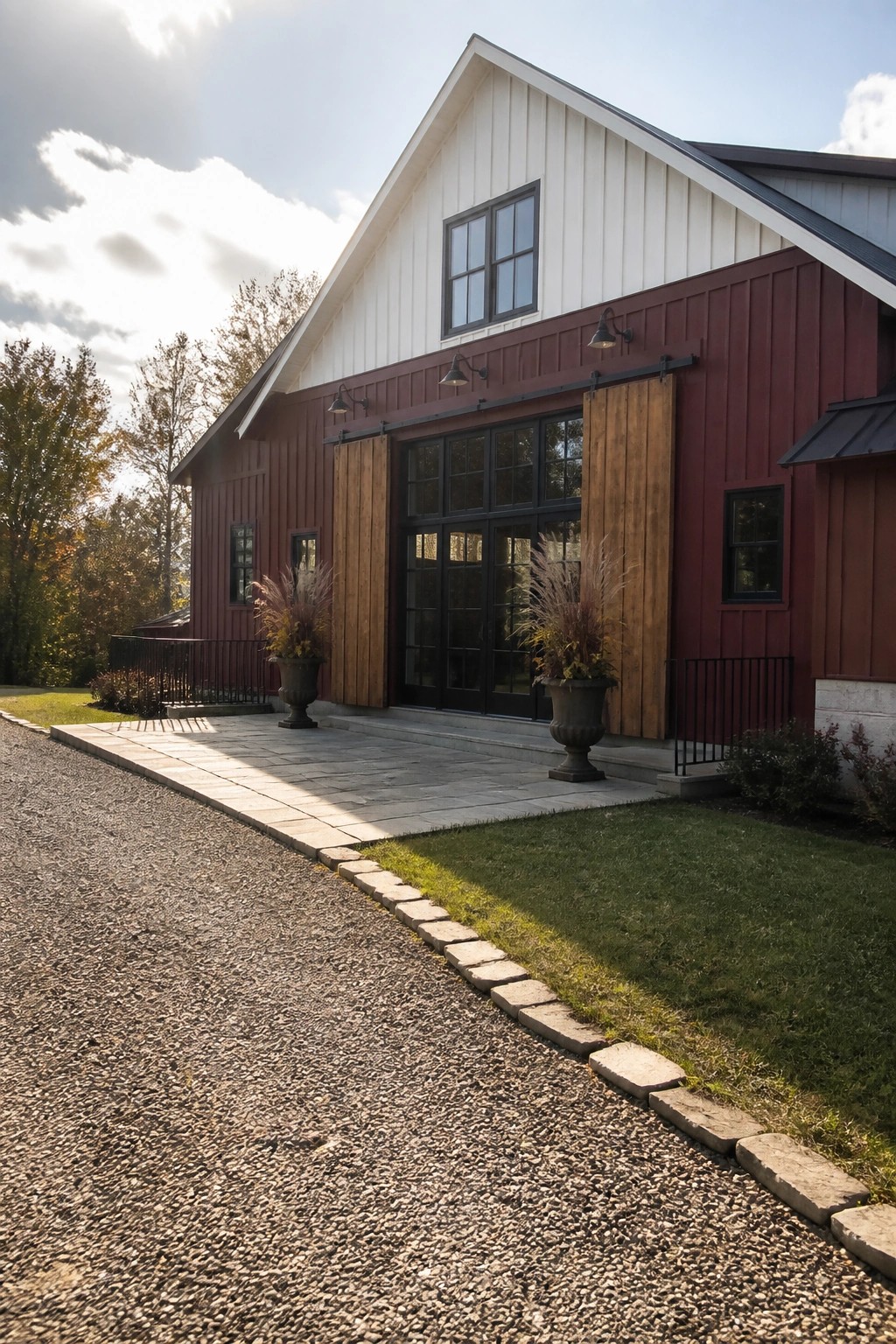 A maroon farmhouse exterior with white board-and-batten on the gable, black-framed glass doors, and wooden sliding barn doors.