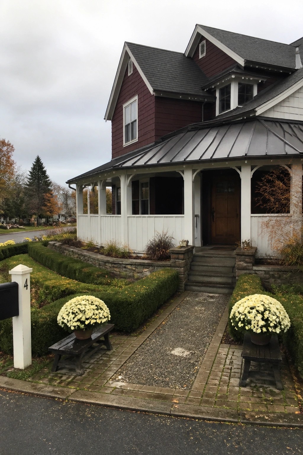 Red house with white porch, two potted yellow flowers on benches, mailbox numbered 4