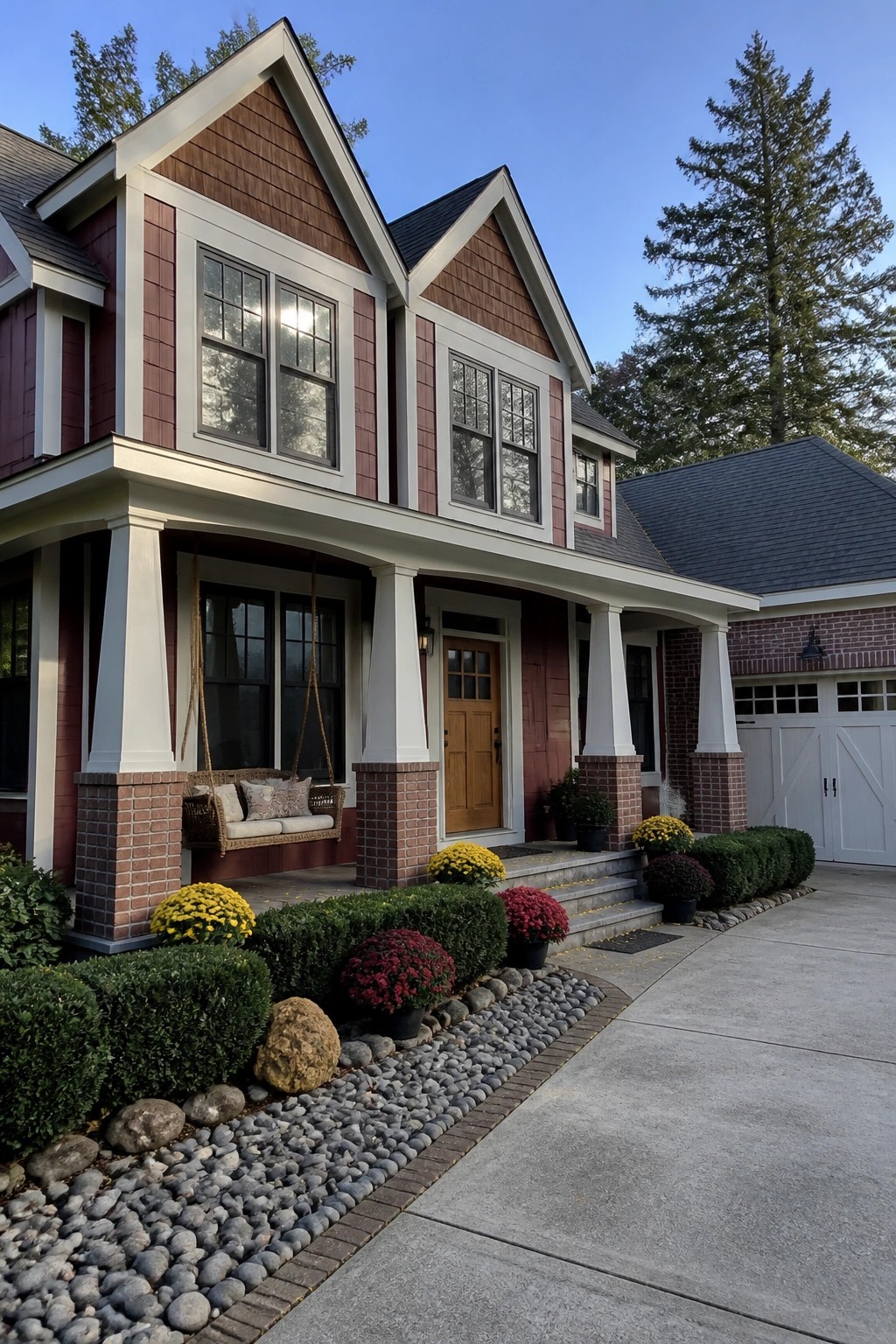 Two-story red house with white porch, swing, brick columns, and flower garden.