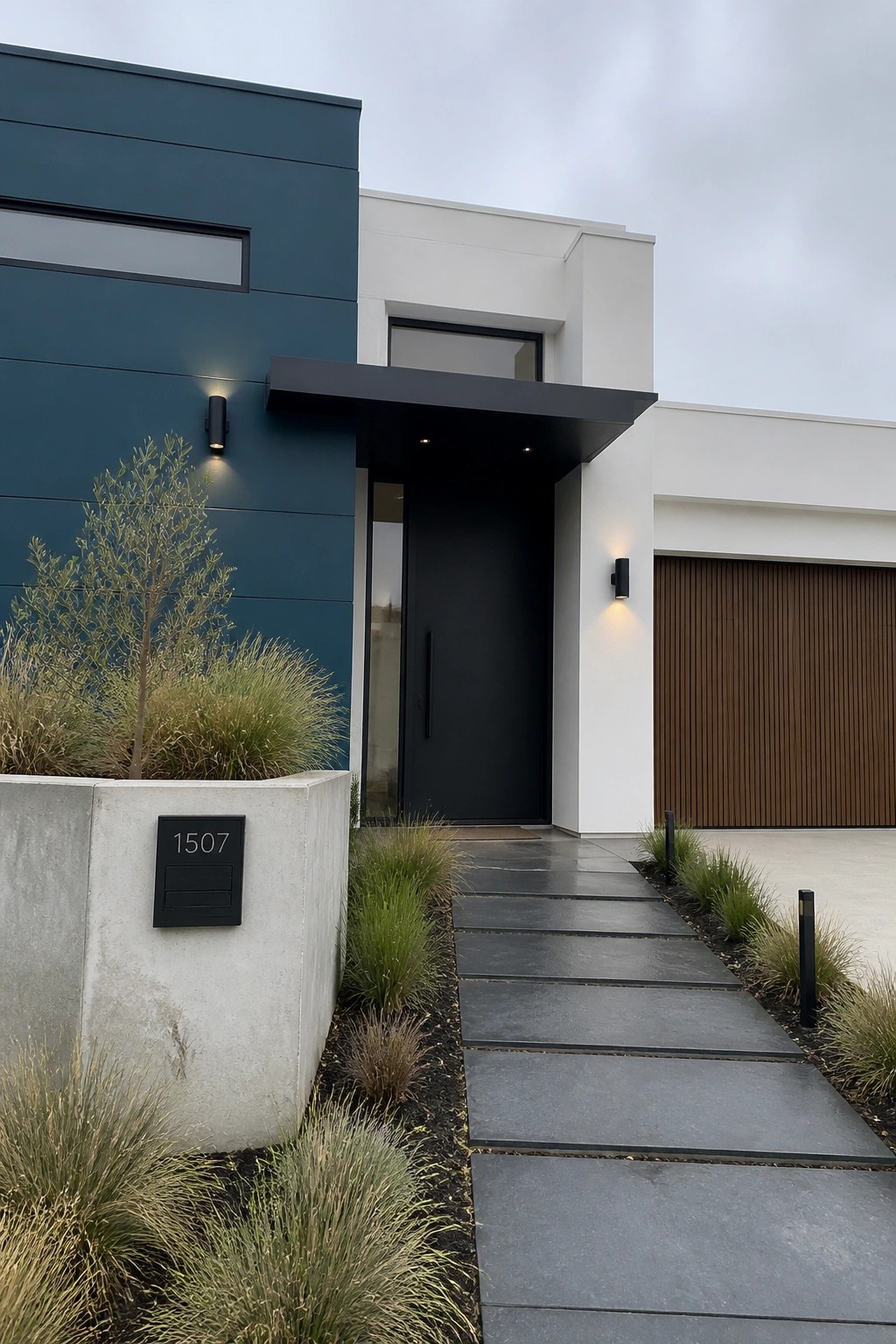 A modern house exterior features large teal panels on the left side next to white walls, a black front door under a black overhang, and a stone pathway leading to the entrance.