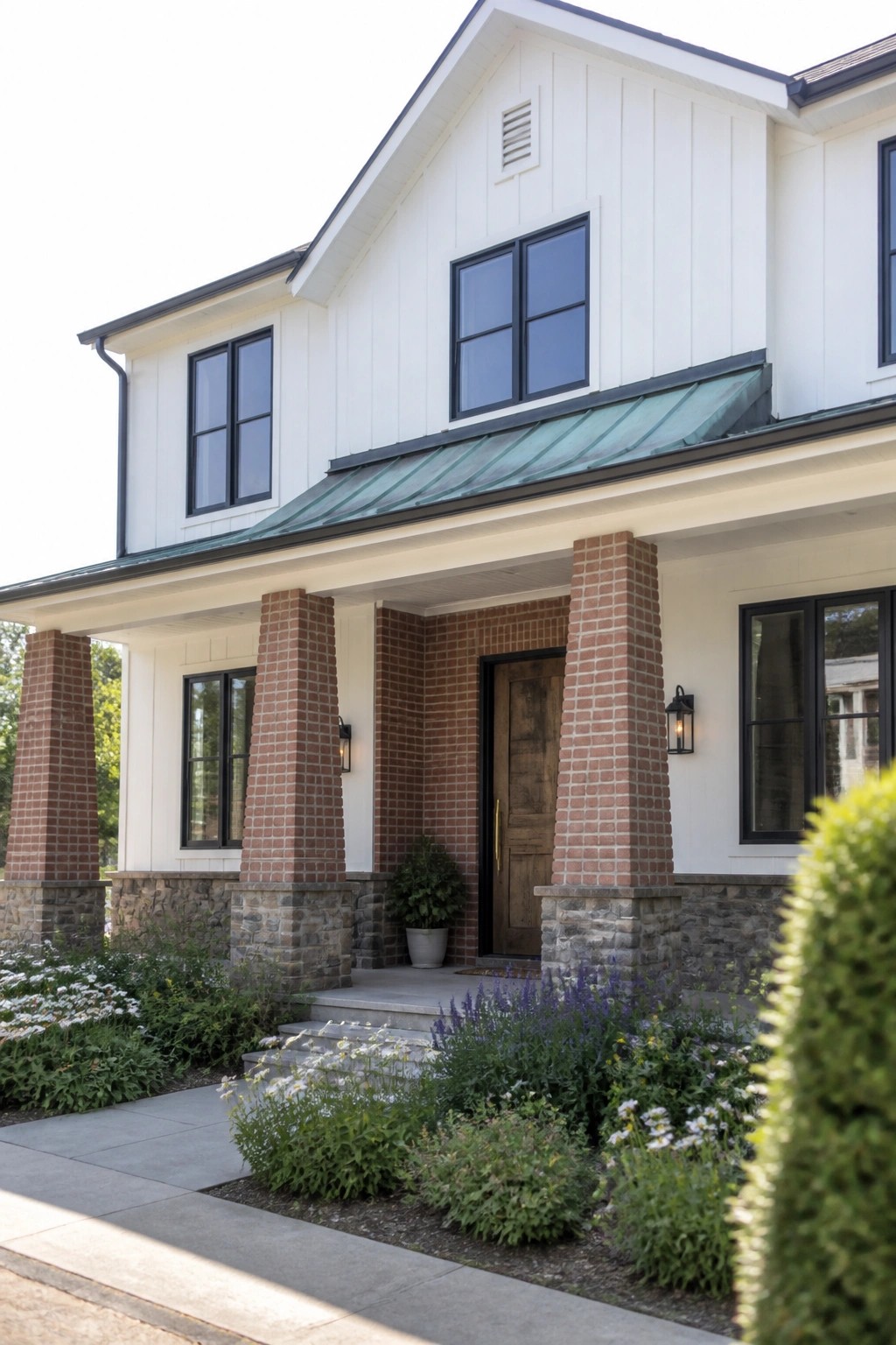 White house exterior with red brick columns flanking a wooden front door under a teal metal roof.