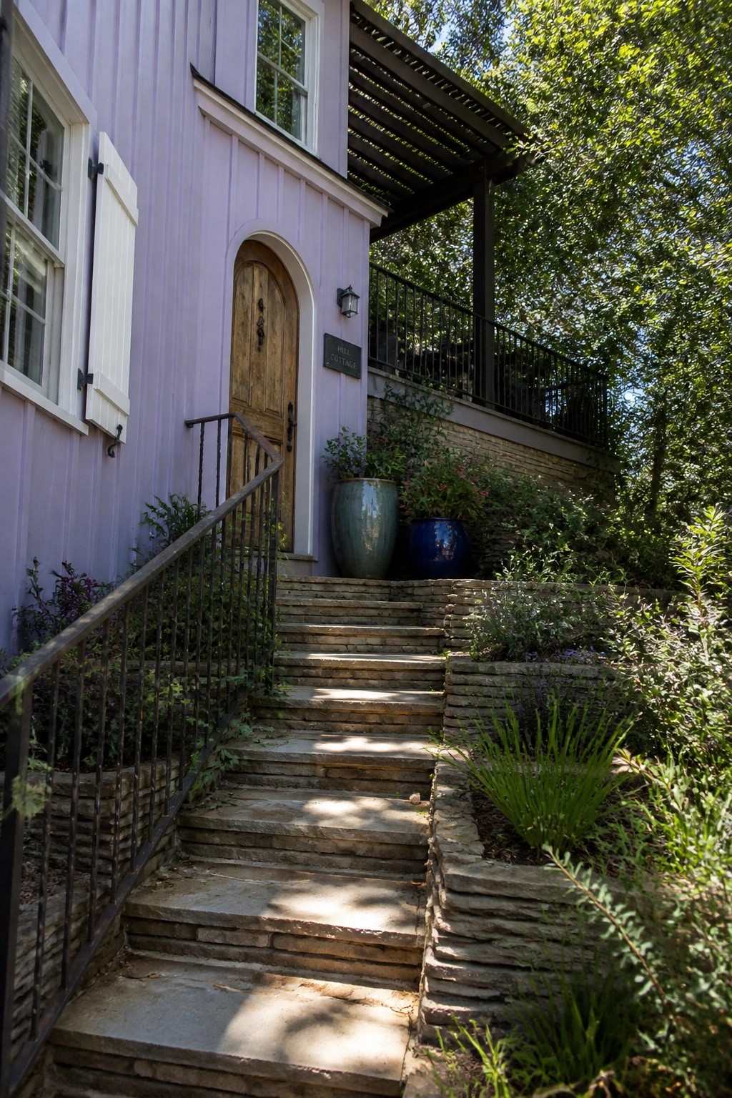 A pastel purple house exterior with white shutters on the windows, a wooden arched door, and stone steps ascending beside it.