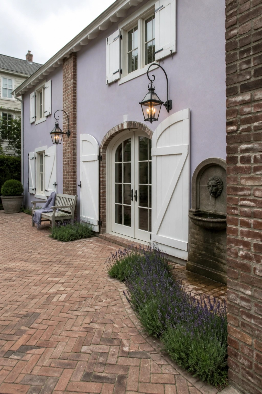 Lavender house with white doors, brick patio, stone lion fountain, and blooming lavender.