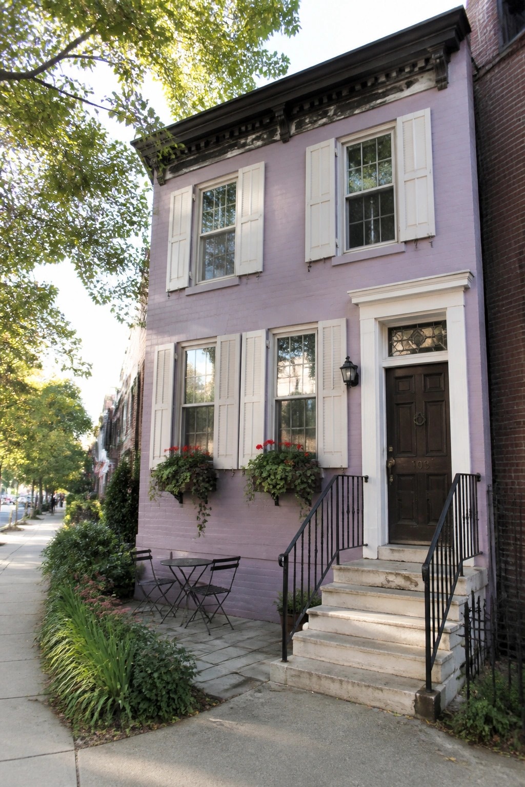 A two-story pastel purple brick house with white shutters on multiple windows, a dark brown door, and stone steps leading to the entrance.