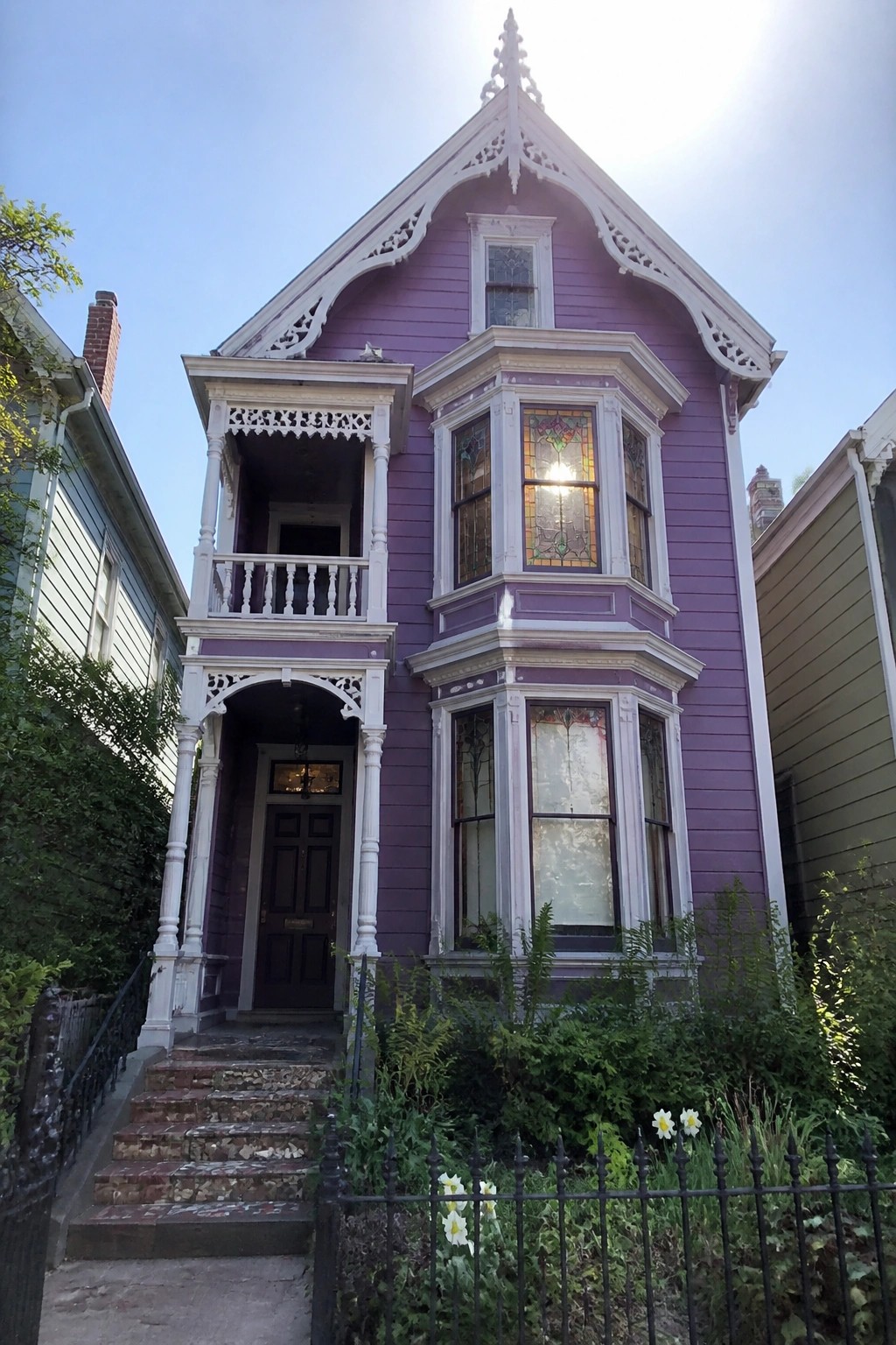 Purple Victorian house with ornate white trim, bay window, and front garden.