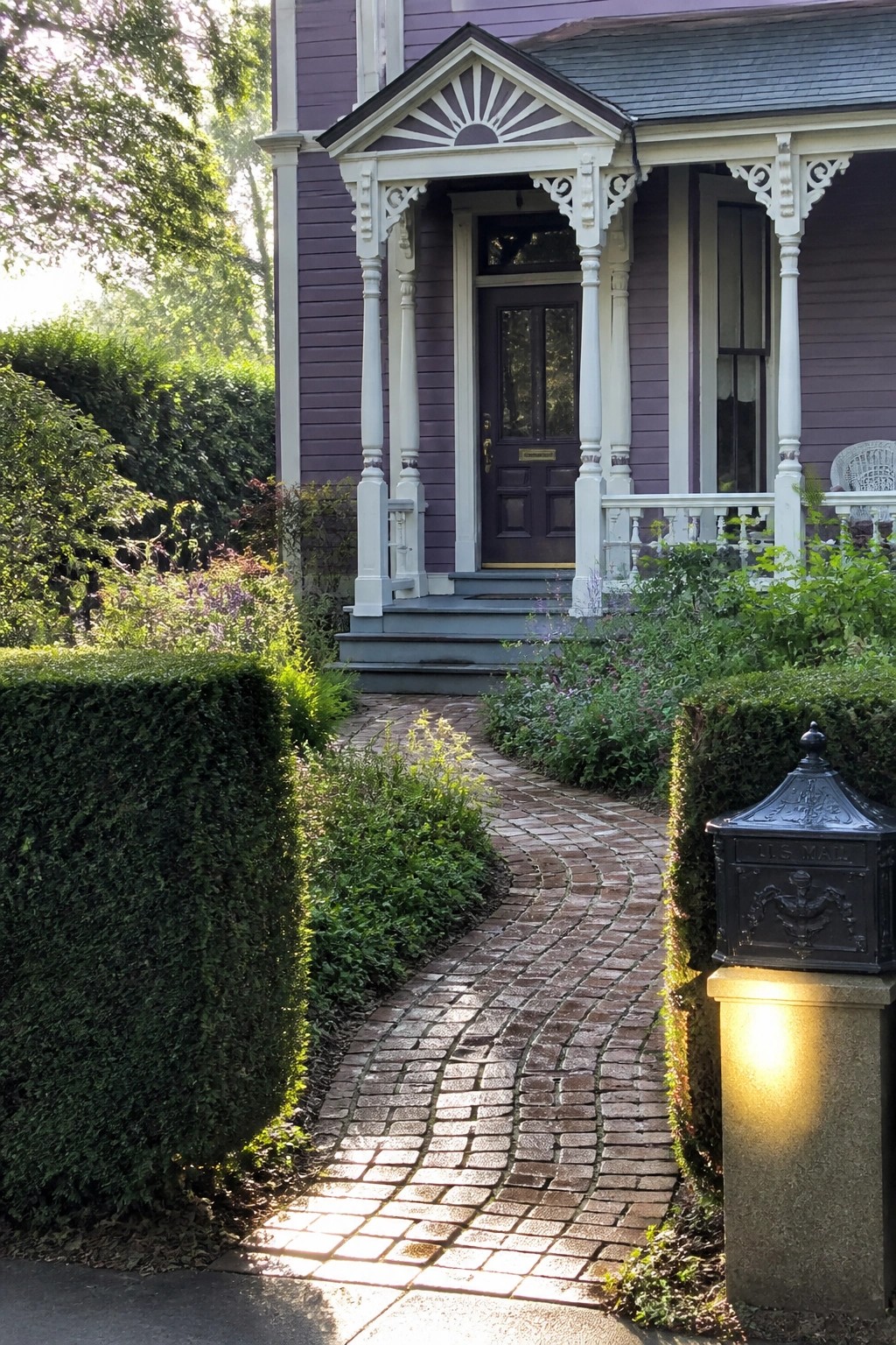 Purple Victorian house with white porch, curved brick path, and black mailbox.