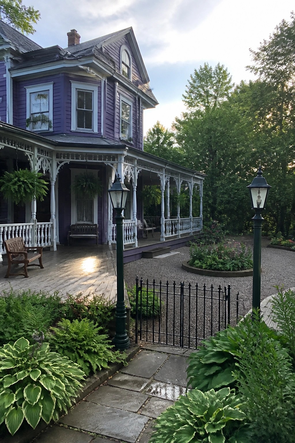Purple Victorian house with white porch, lush garden, lampposts and gravel path.