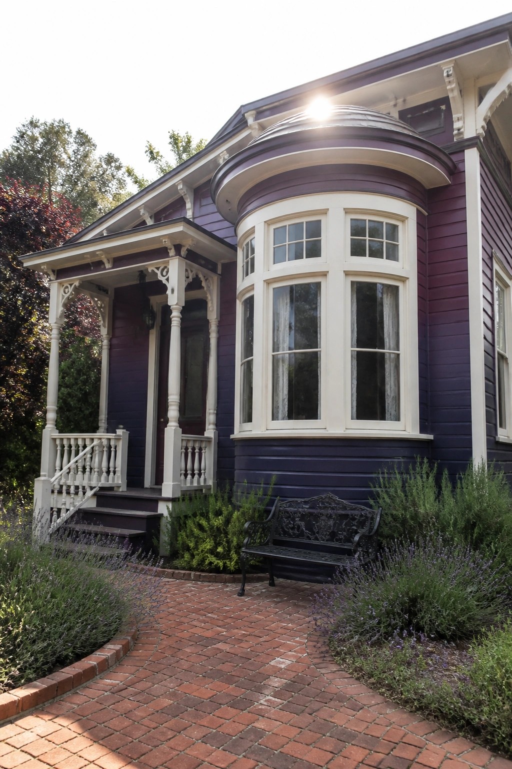 A purple Victorian house exterior with ornate white trim, a bay window, front porch, and brick pathway lined with lavender plants.
