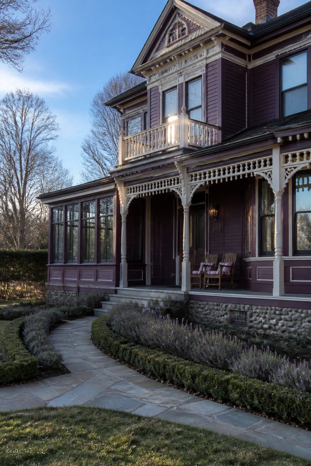 A purple Victorian house exterior with ornate white trim, a front porch with two chairs, and a stone pathway leading to the entrance.