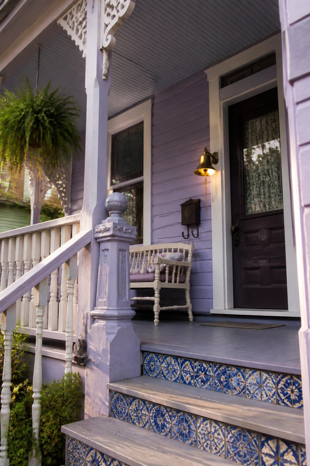 Front view of a purple Victorian house porch with ornate white trim, a wooden bench, tiled steps, and a dark front door.