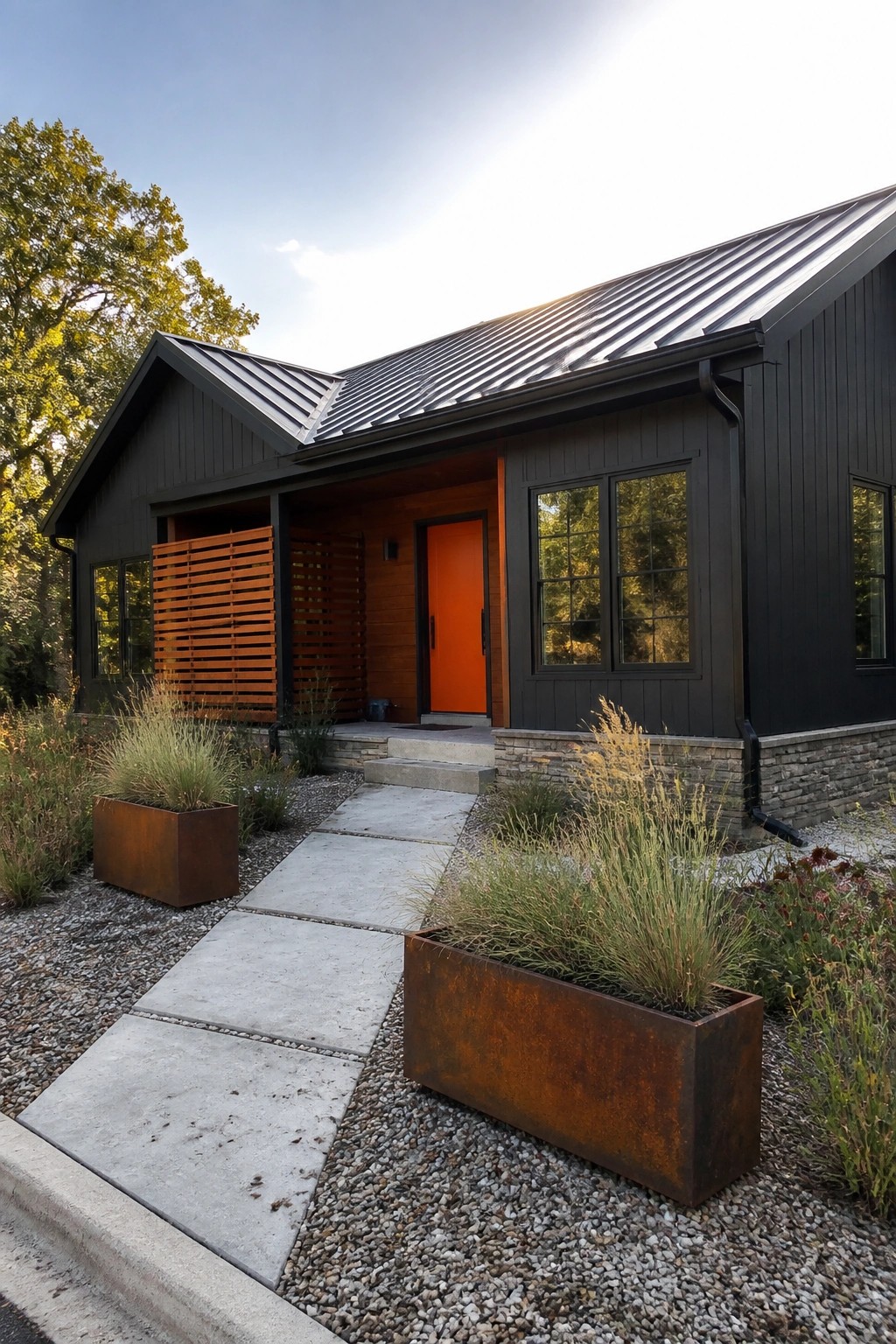 A front view of a modern house with black vertical siding, an orange door, a charcoal metal roof, and rusted metal planters along a concrete walkway.