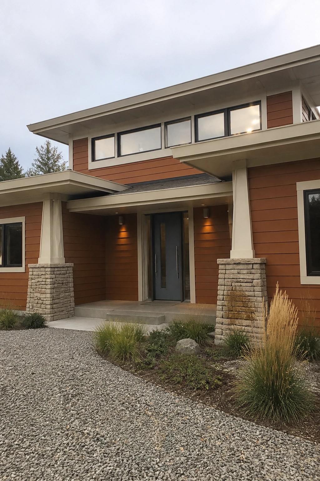 Modern house with orange-brown siding, blue door, stone pillars, and gravel driveway