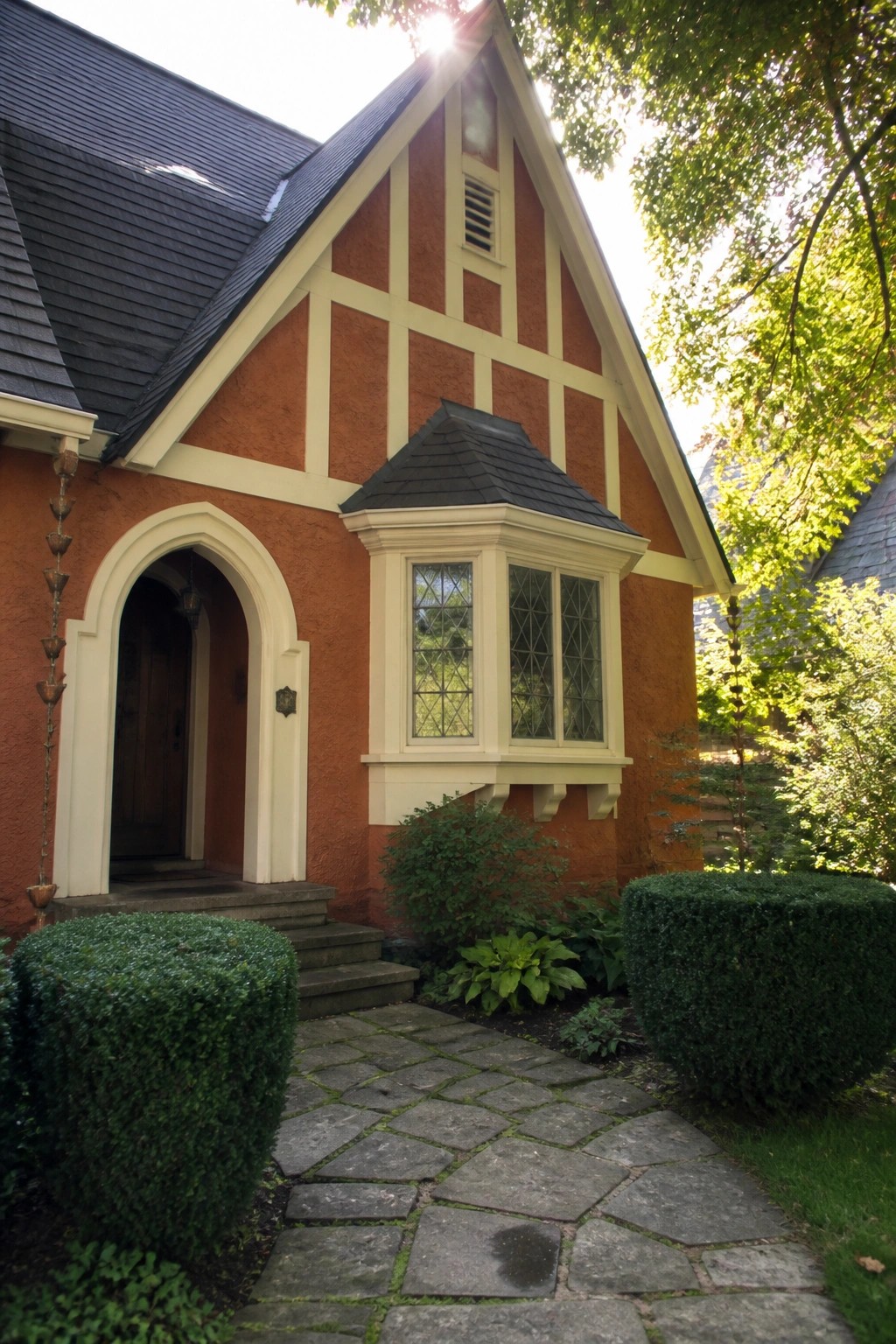 Orange Tudor house with white trim, arched doorway, bay window, stone path.