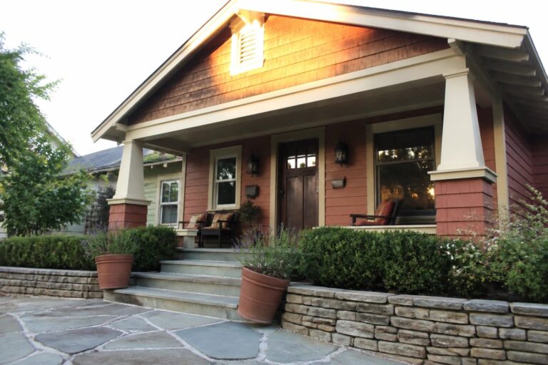 A front view of a house with burnt orange siding, cream trim on the porch columns and eaves, a dark wood door, and a stone path leading to the steps.