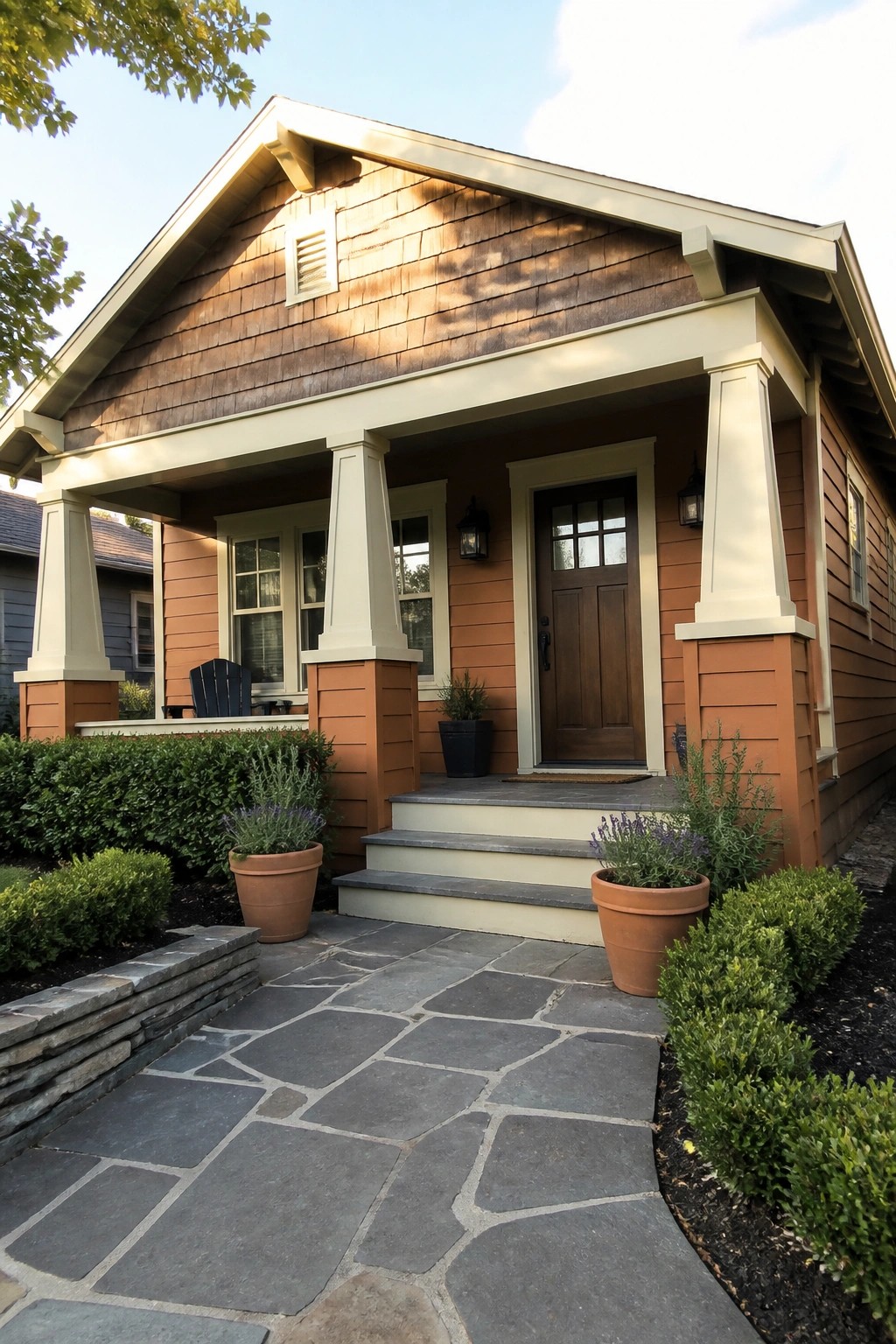 A front view of a house with burnt orange siding, cream trim on the porch columns and eaves, a dark wood door, and a stone path leading to the steps.