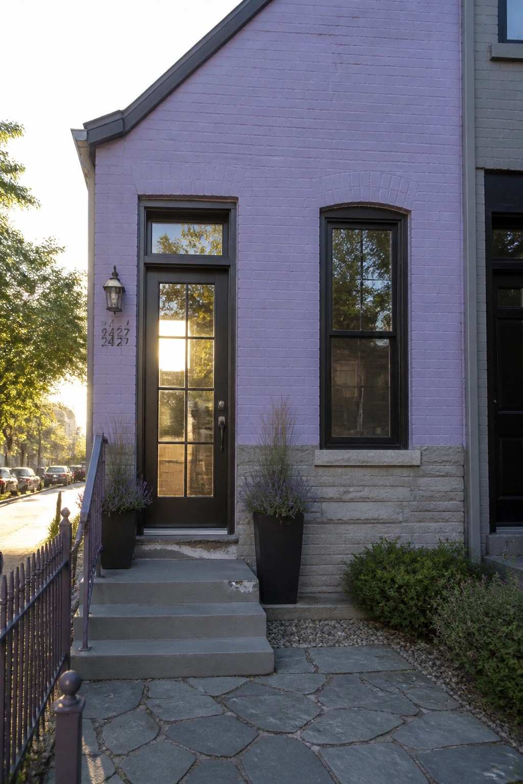 Purple brick house entrance with black door, arched window, and potted plants