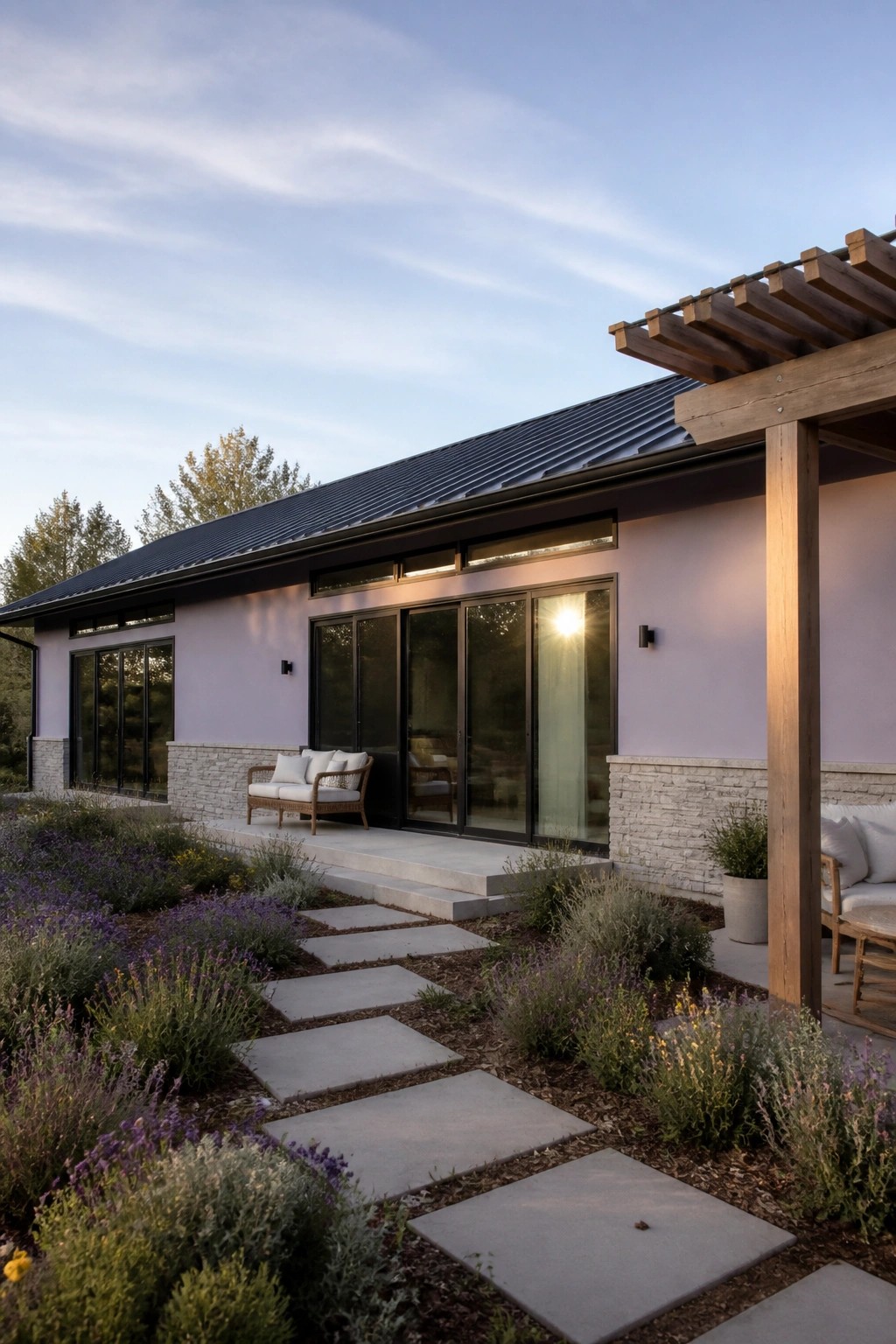 A lavender house exterior with stone veneer base, black-framed sliding doors, concrete steps, and a wooden pergola beside a stone path through garden beds.
