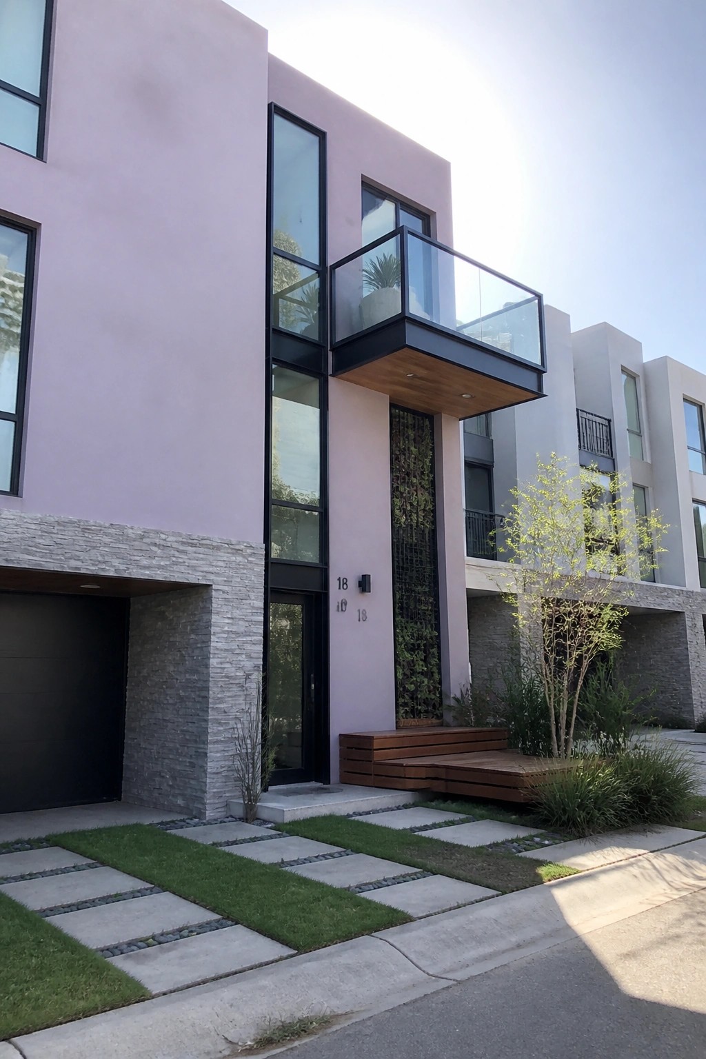 A modern two-story house with lavender stucco walls, gray stone on the lower sections, black window frames, and a cantilevered balcony with glass railing.