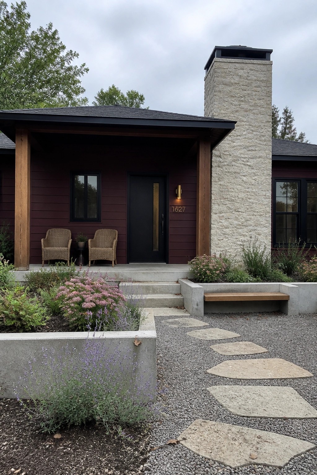 A modern house with deep burgundy fiber cement siding, a black front door with vertical gold handle, wood porch posts, and a tall light stone chimney.