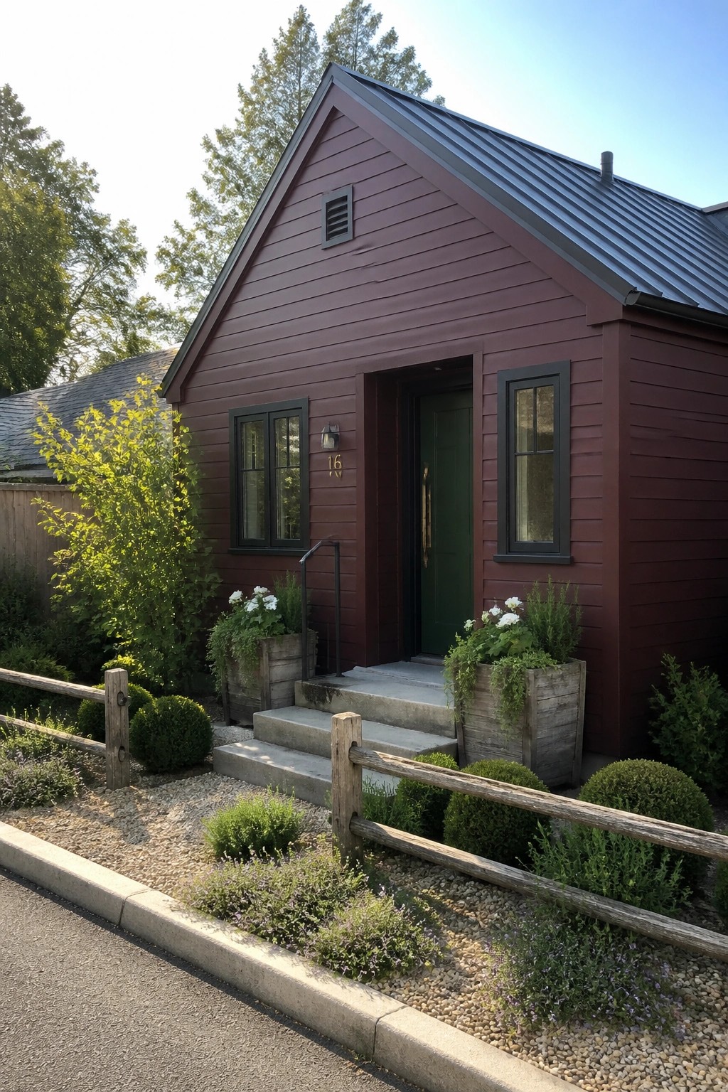 A small burgundy house with smooth fiber cement siding, black window frames, a green door, concrete steps, and wooden planters along the front.