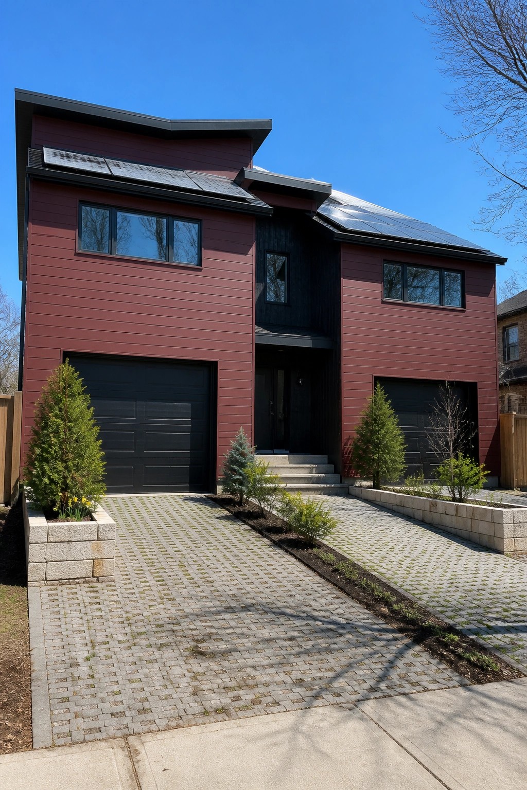 A modern two-story house with horizontal maroon fiber cement siding, black garage doors, black trim, and solar panels on the roof.