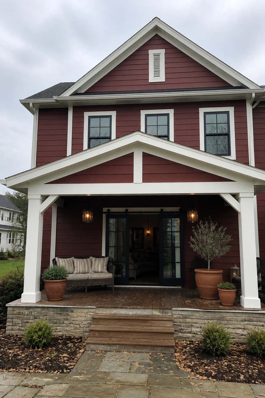 A two-story house with maroon fiber cement siding, white trim around windows and gables, a covered front porch, and wooden steps.