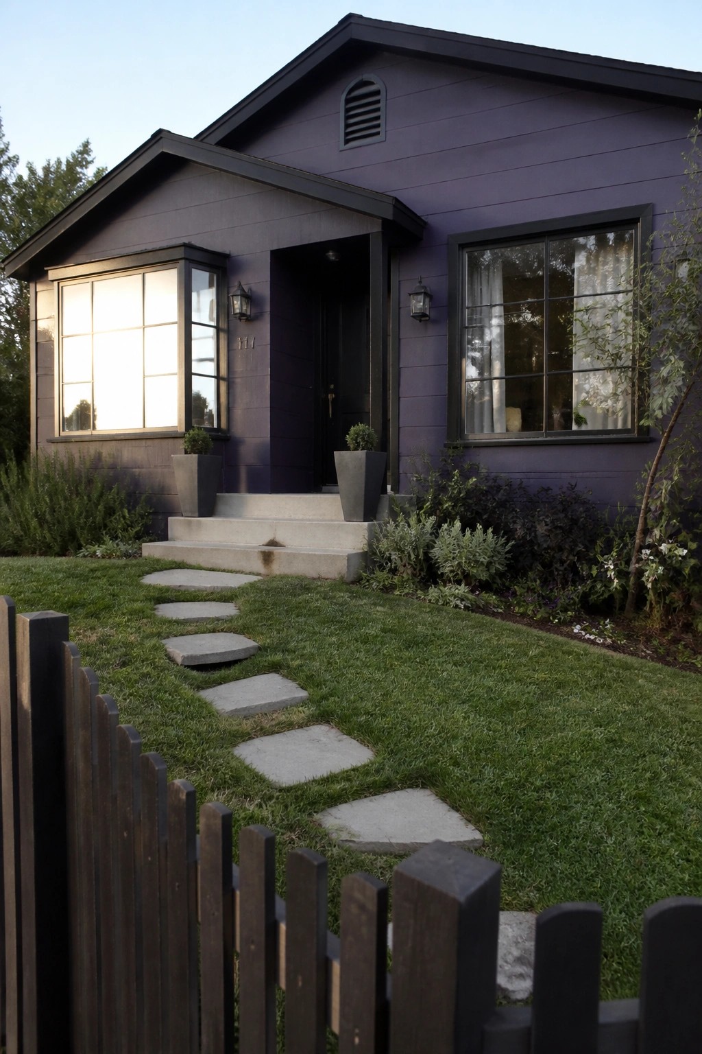 A single-story house with deep purple horizontal siding, black window frames, a black front door, and concrete steps leading to the entrance.