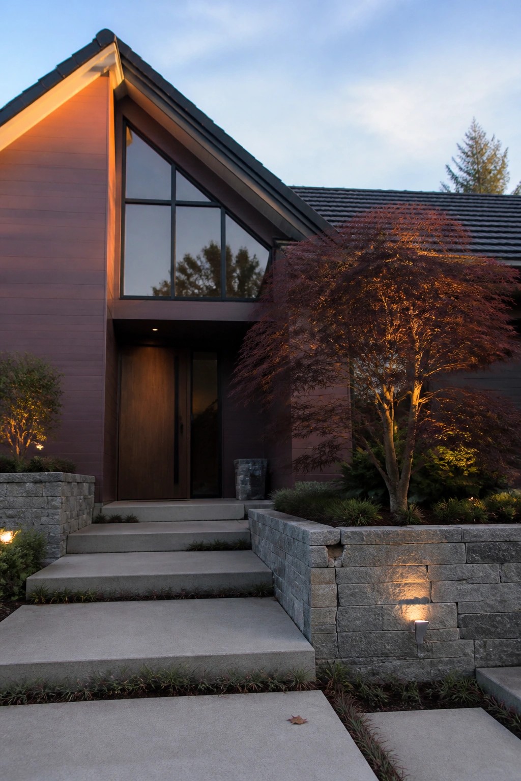 Modern house with large triangular window, wooden door, lit red maple tree at dusk