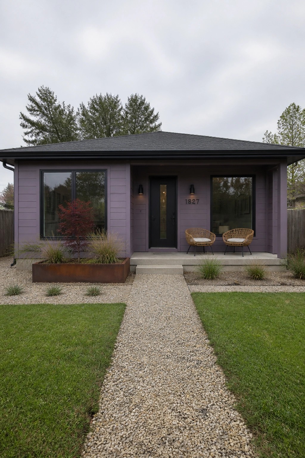 A single-story house with smooth purple siding, black-framed windows, and a black front door, with a gravel path leading to a small concrete porch.
